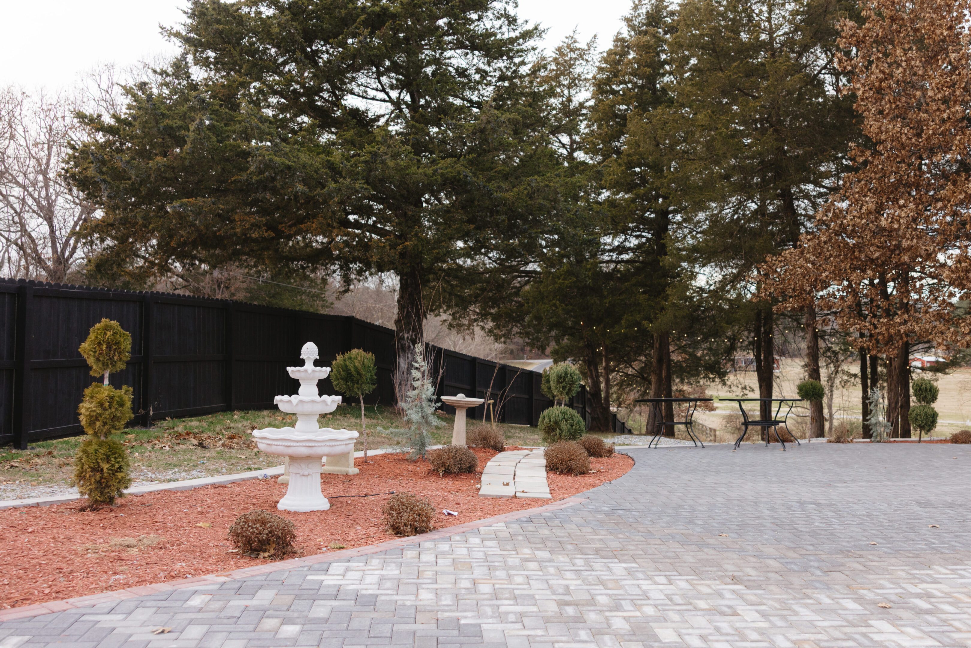 A serene outdoor garden with a white fountain and tall trees.
