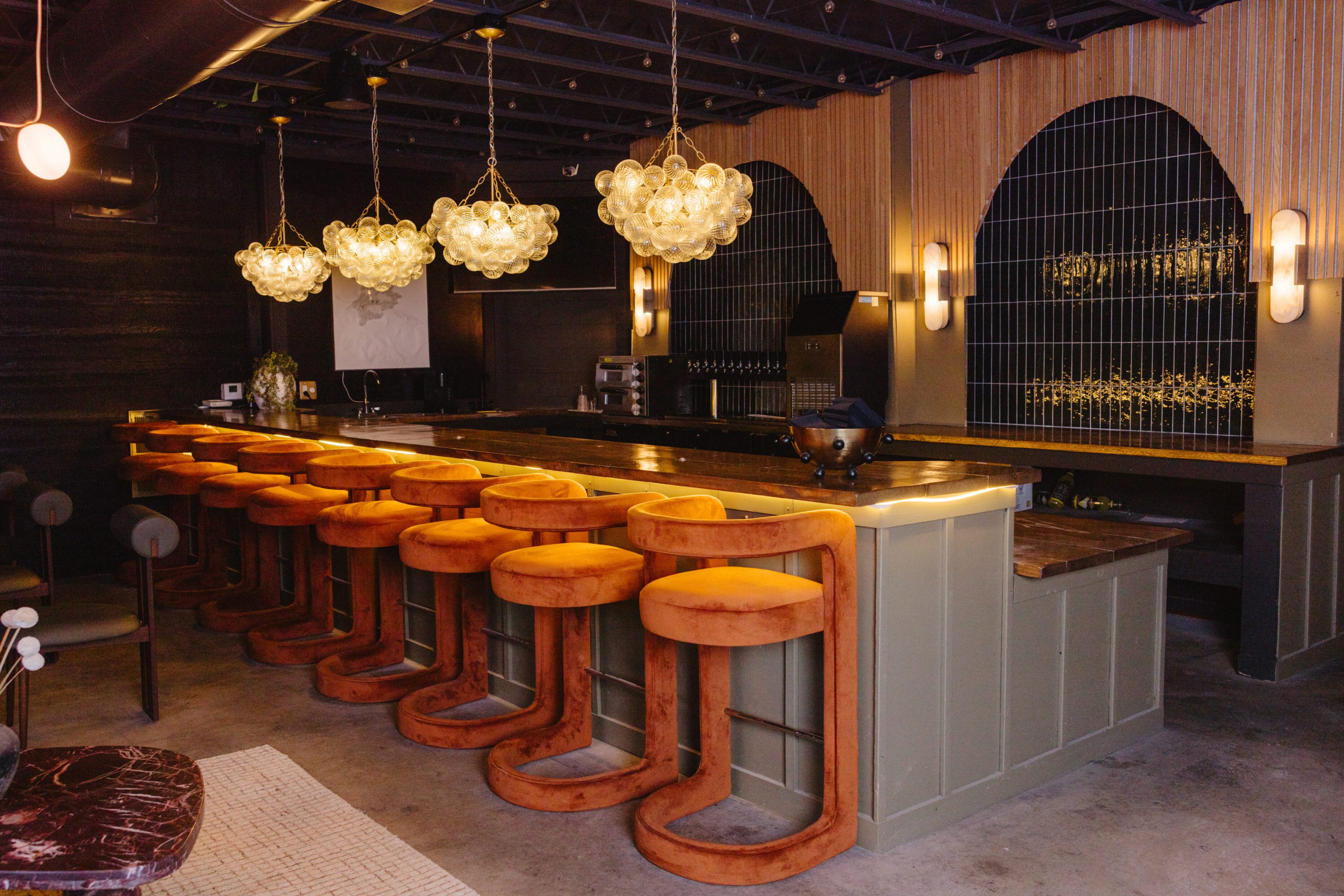Elegant bar with orange swivel stools and ornate chandeliers.