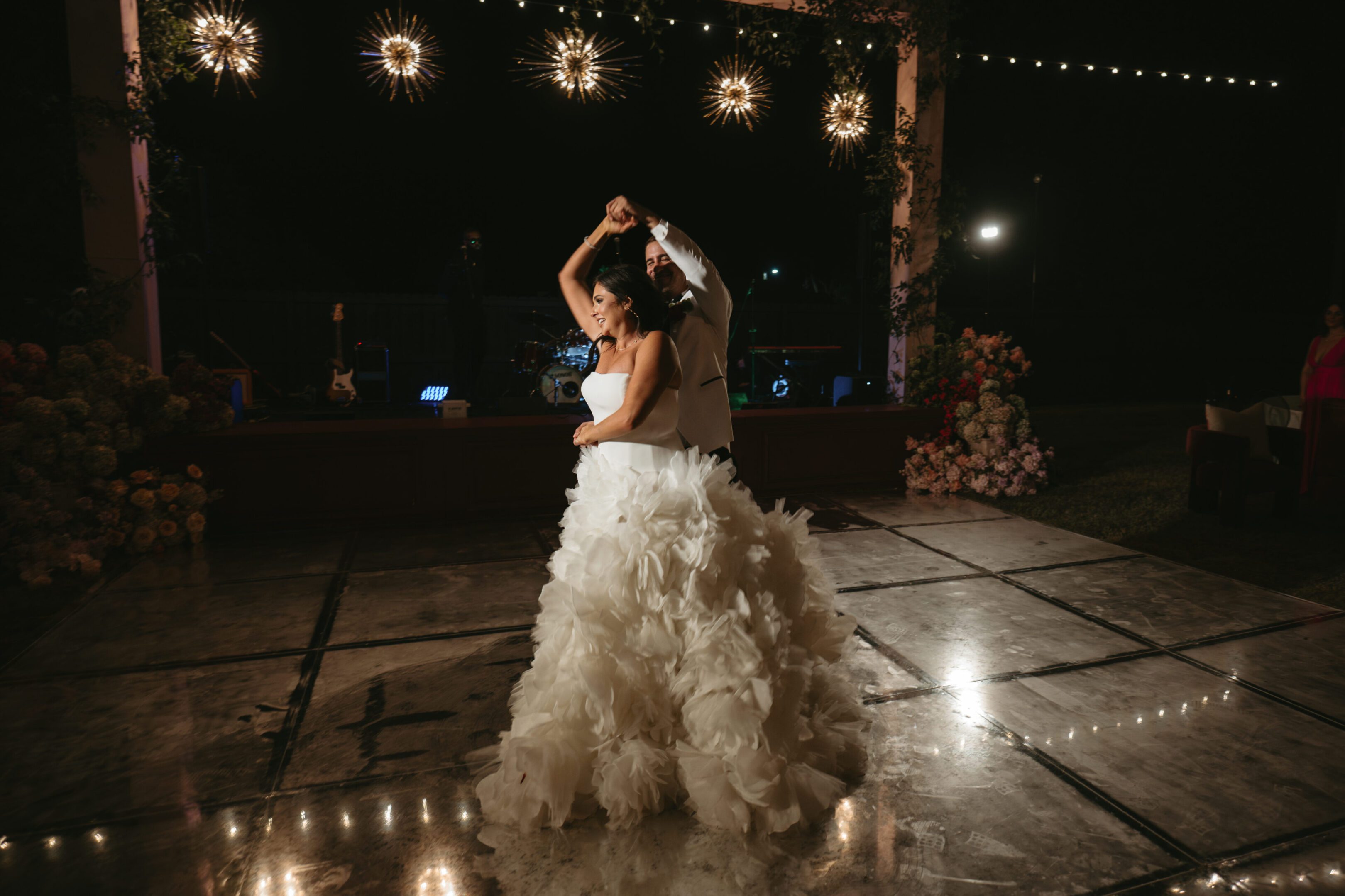 Bride dancing alone on a decorated outdoor dance floor at night.