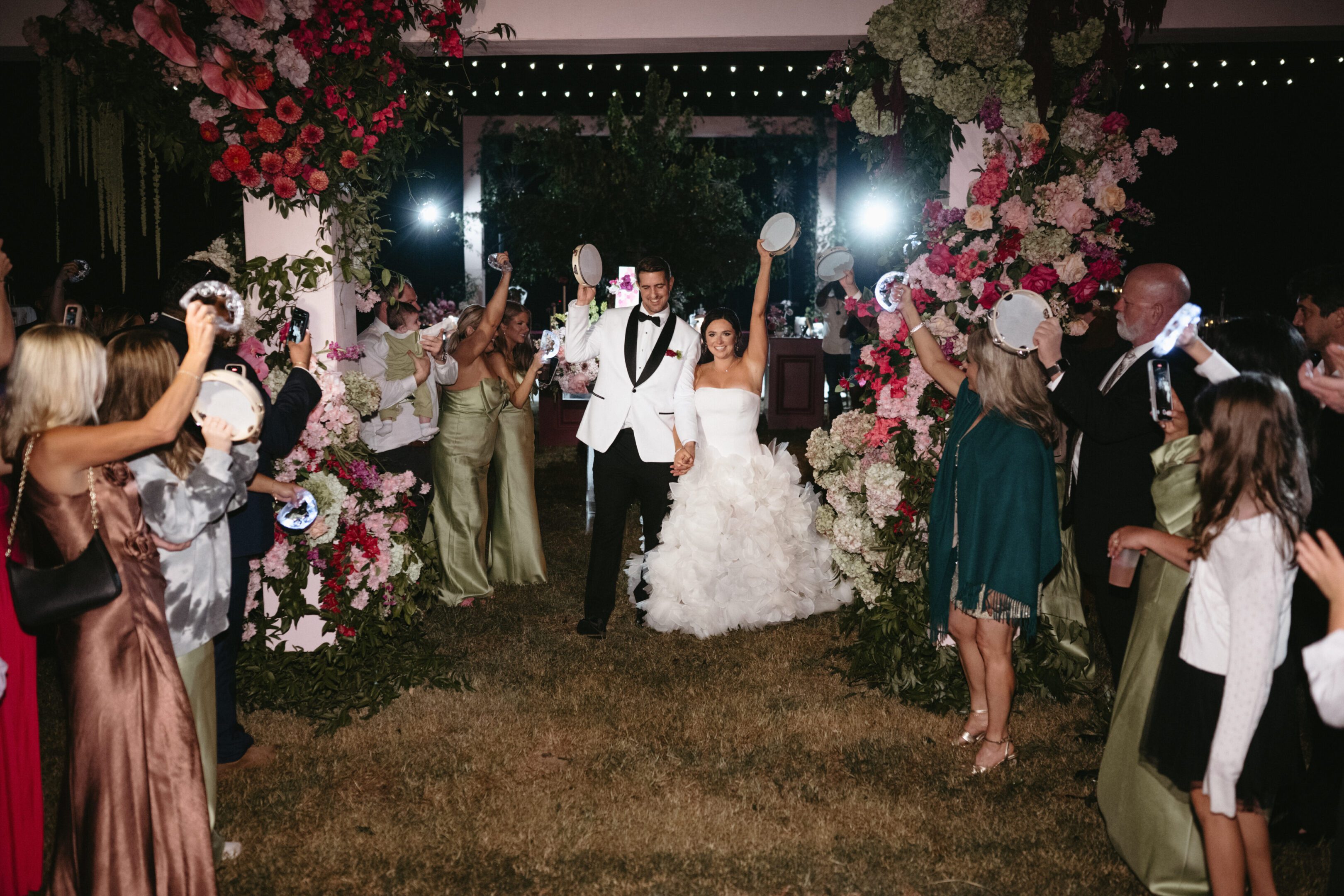 Bride and groom joyfully exit under a floral arch with cheering guests.