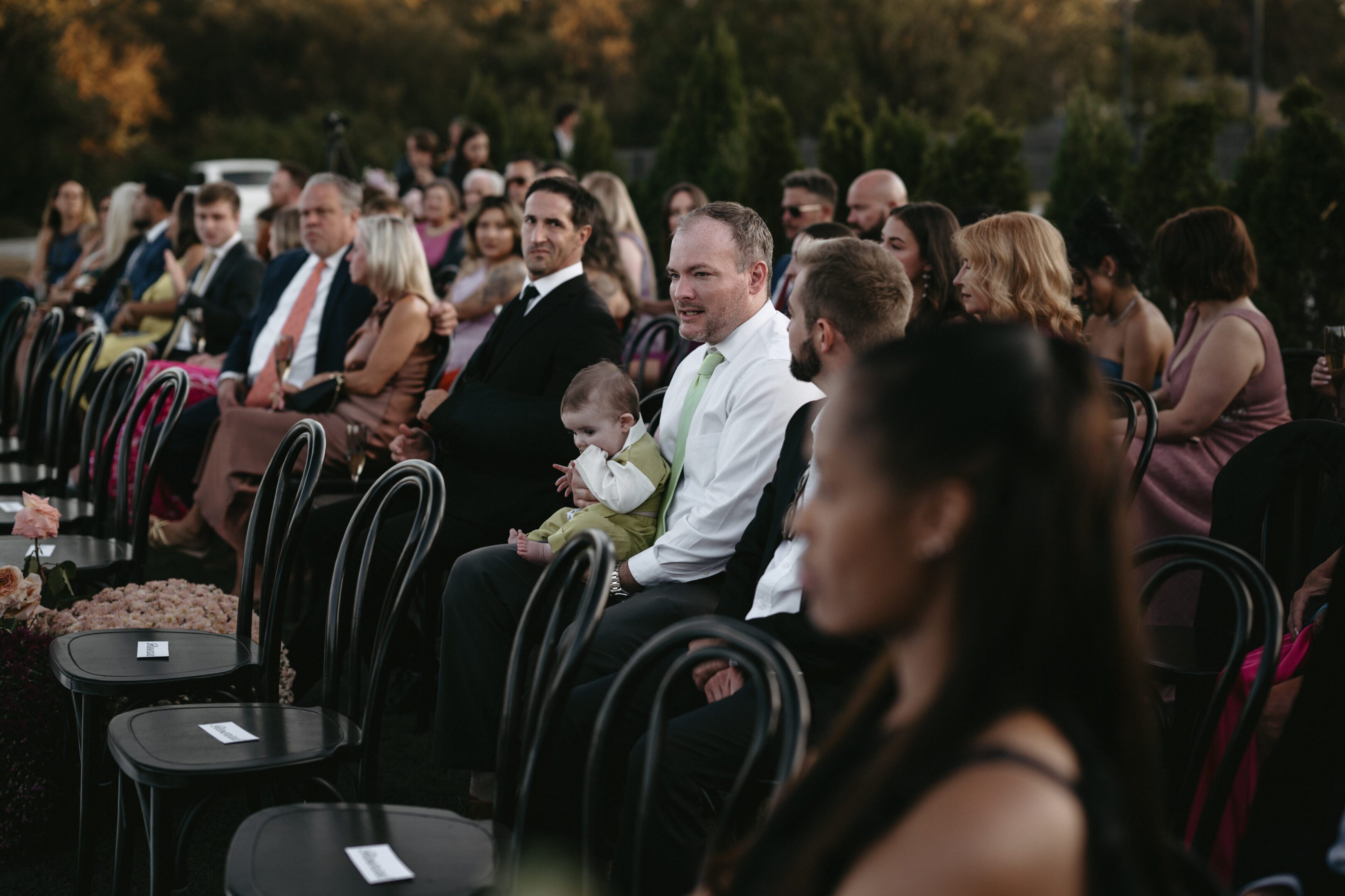 People seated, attentively watching an event outdoors during the day.