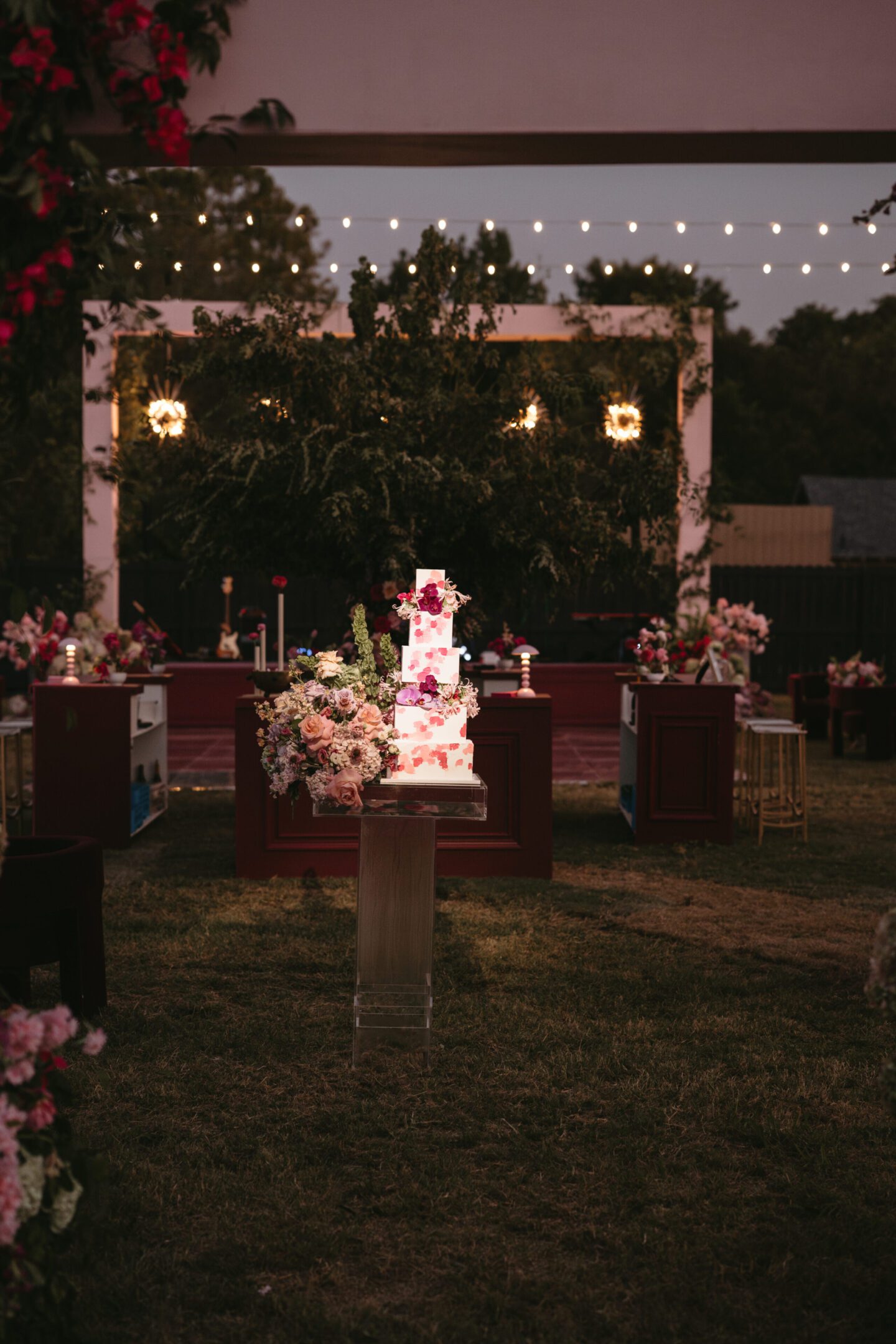 Outdoor wedding reception setup with floral decorations and string lights.