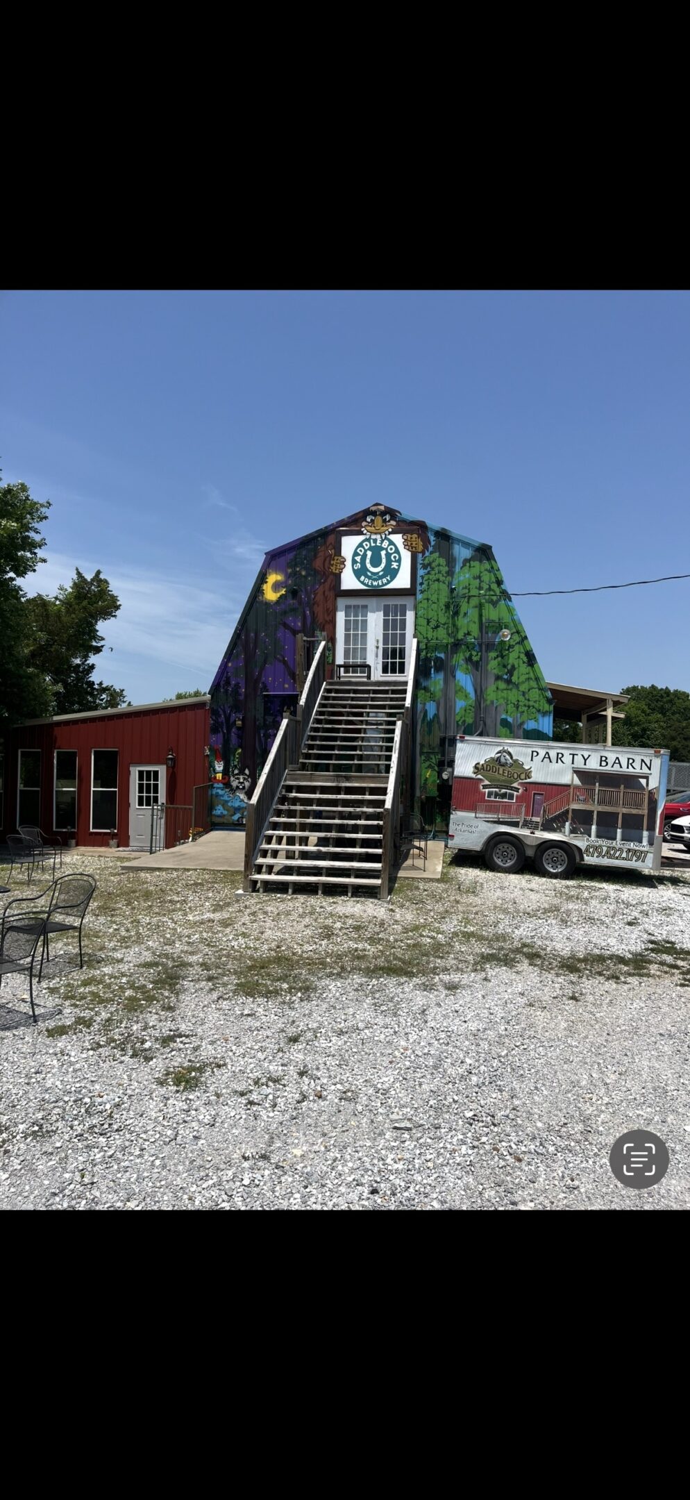 A colorful building with stairs and a trailer in a gravel lot.