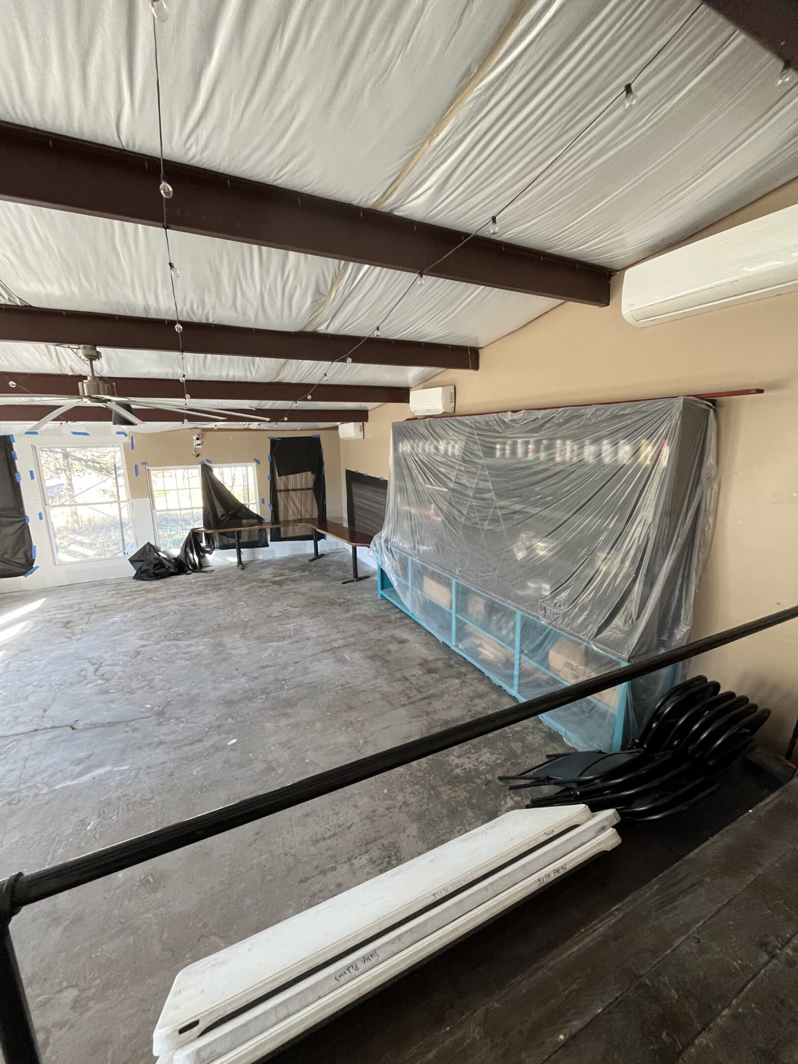 An empty room with construction materials and plastic-covered items under a wooden ceiling.