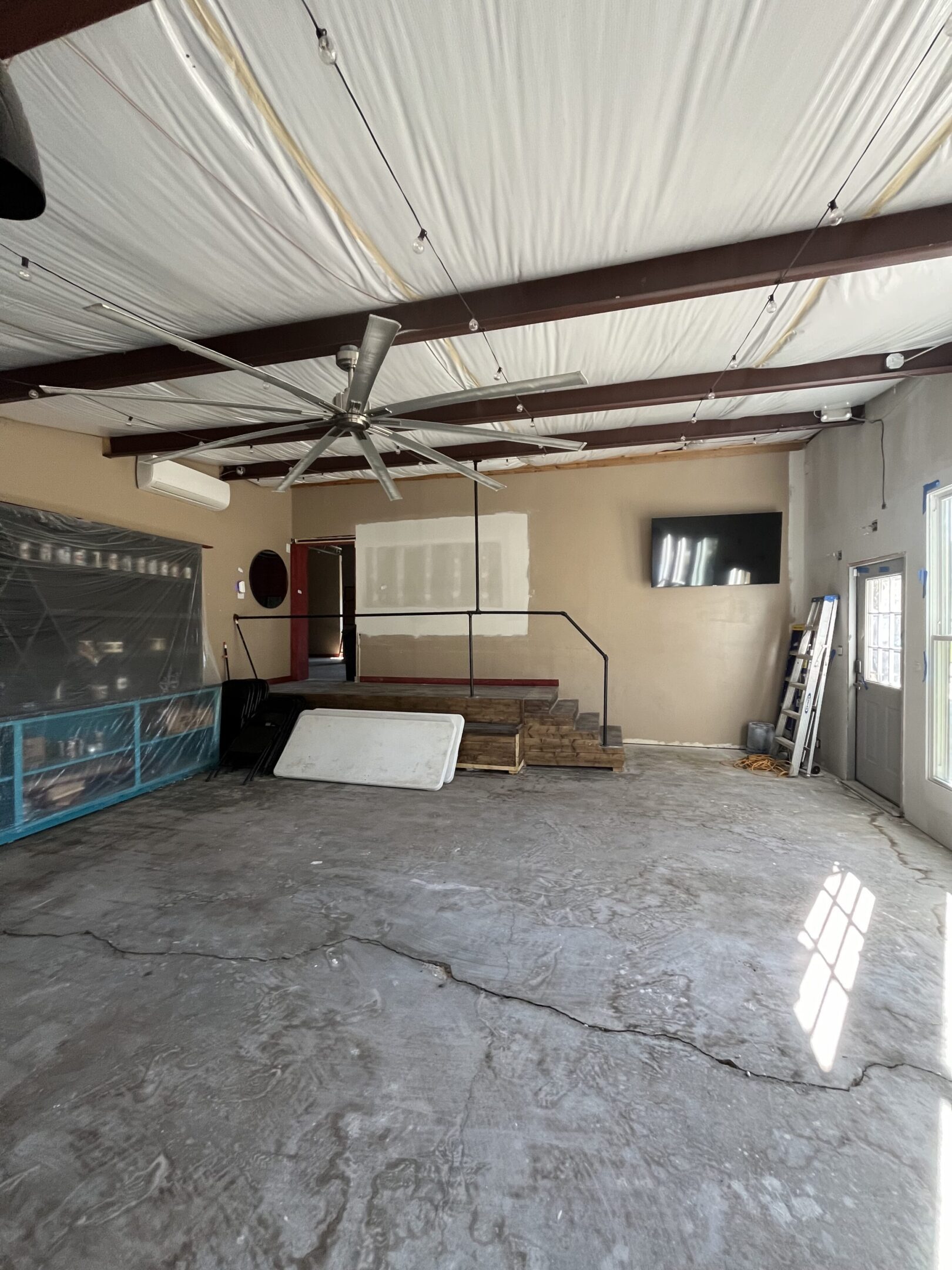 Empty room with exposed beams, whiteboard, and some scattered furniture.