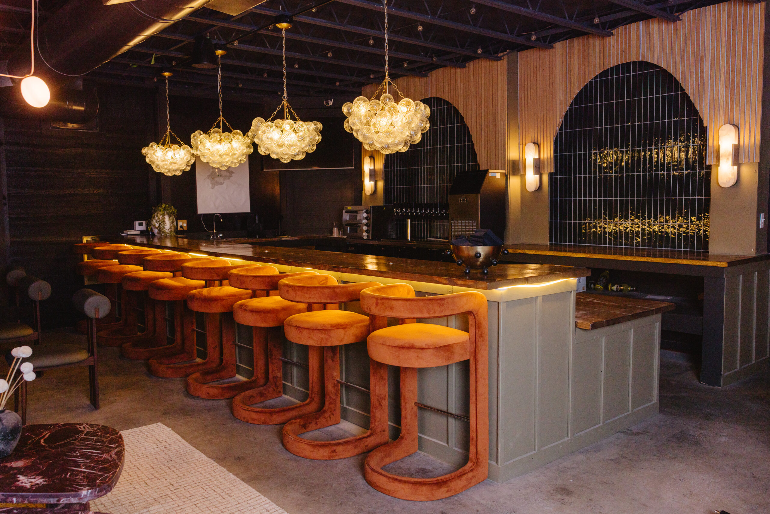 Elegant bar with orange stools and floral chandeliers.