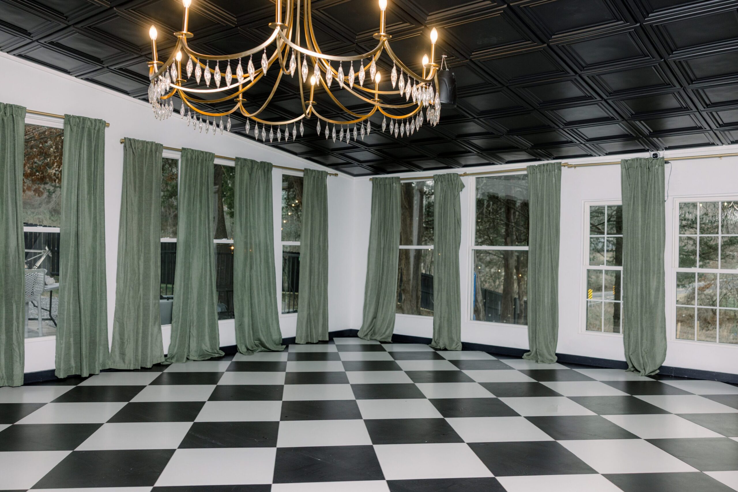 Elegant room with checkered floor and green curtains under a chandelier.