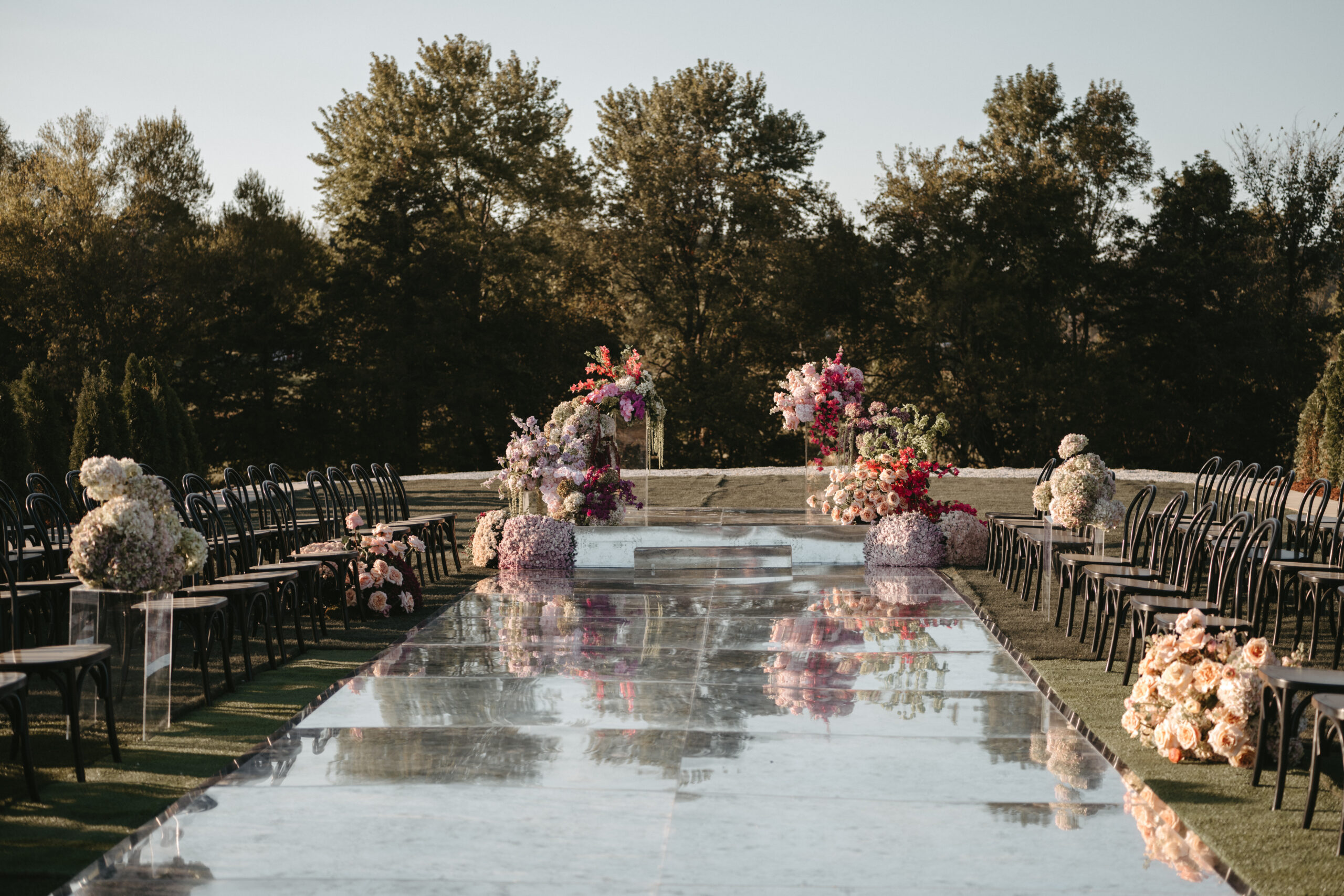 Elegant outdoor wedding aisle with floral arrangements and reflective walkway.