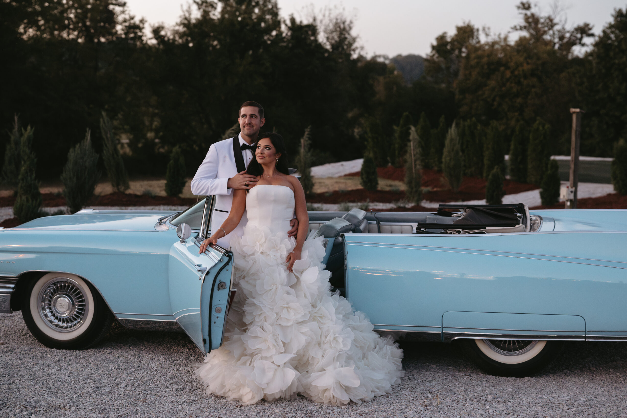 Bride and groom posing with a vintage blue car outdoors.