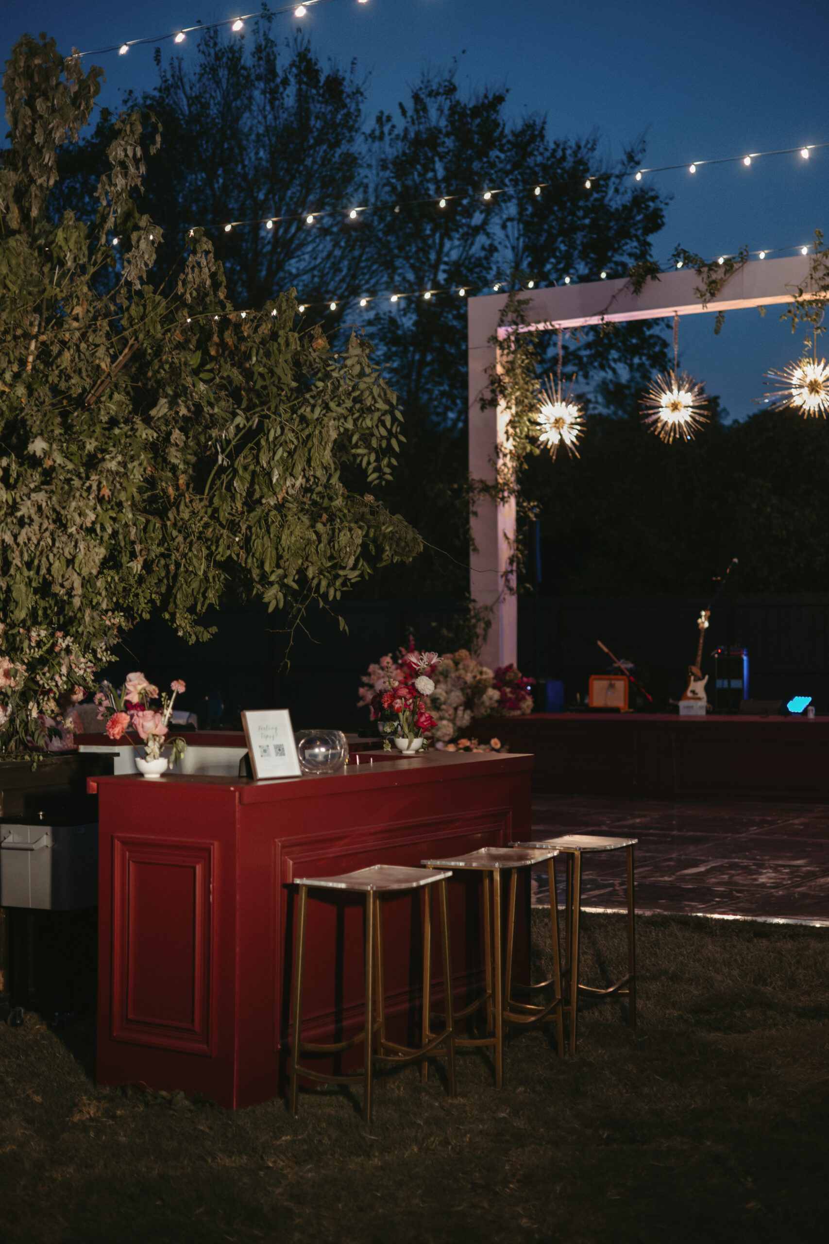 Elegant outdoor bar setup with floral decorations and hanging lights at night.